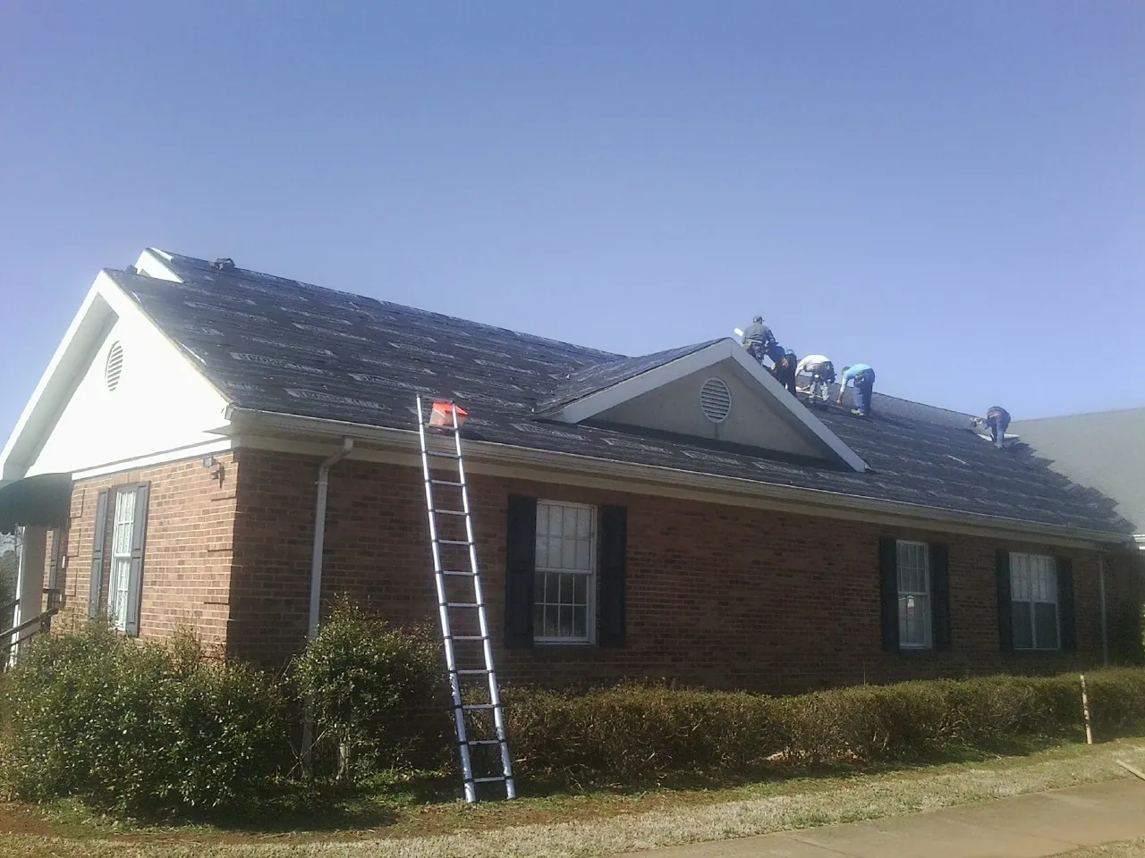 Crew tearing shingles off a brick ranch roof with a ladder set — Emergency Roof Repair work by our crew in Carpinteria