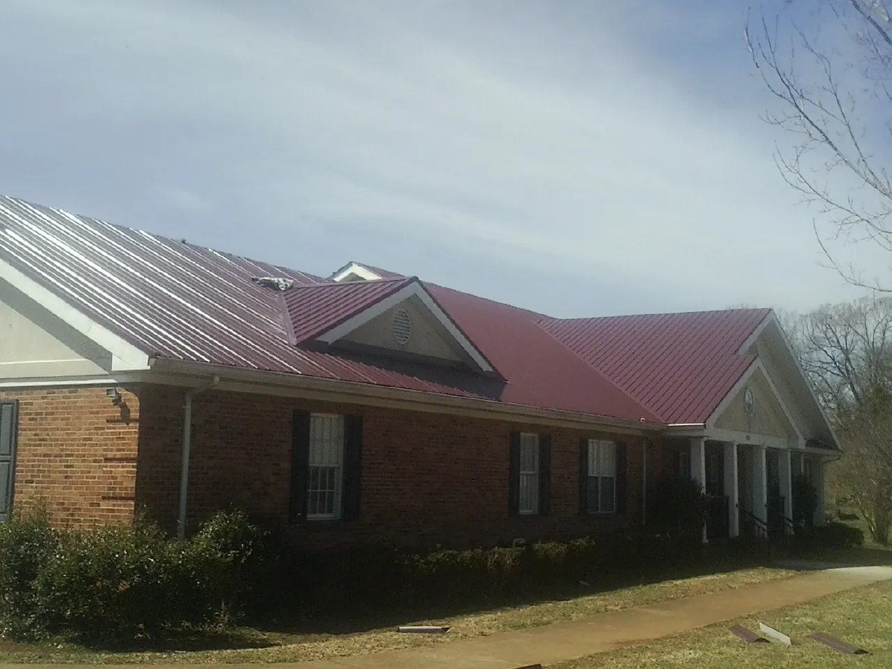 Red metal roof with gabled entries on a long brick building, from a Hail Damage Roof Repair job in Carpinteria