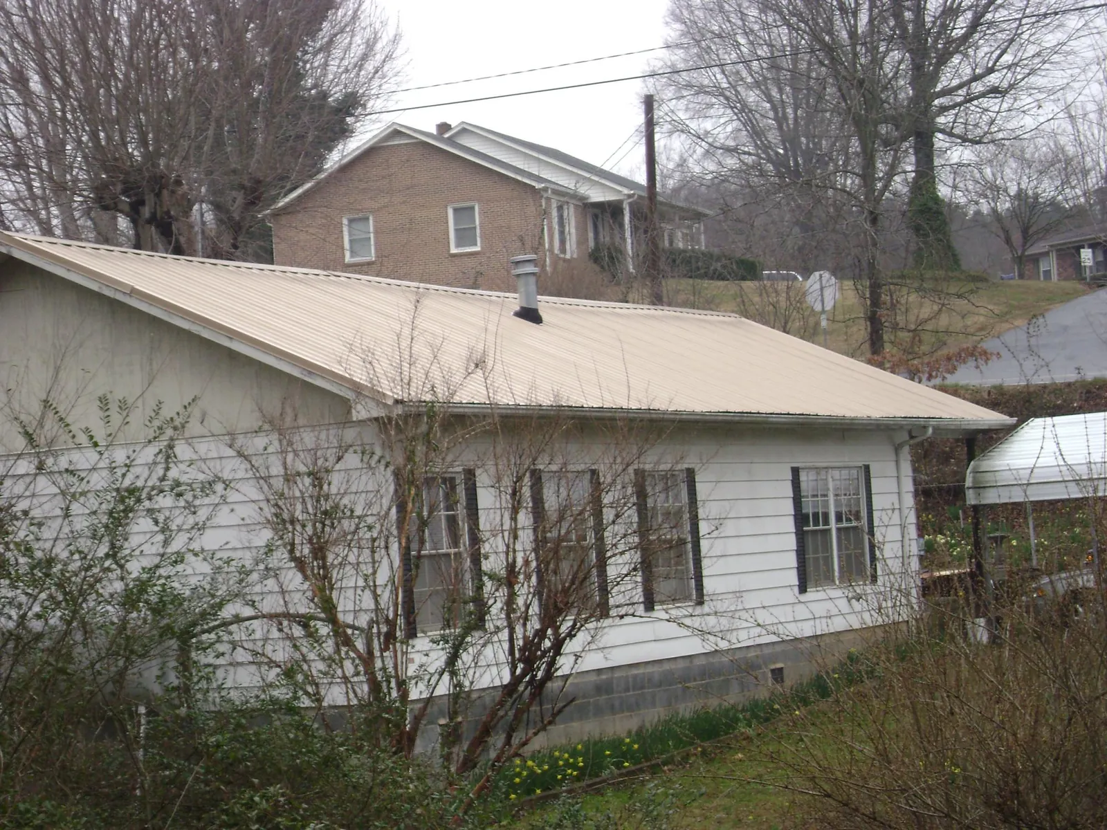 Tan metal roof on a white sided house set into a hillside — Commercial Roofing by Roofing Brothers in Carpinteria